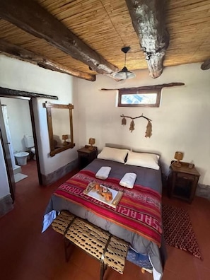 Una habitación con cama, ventilador de techo, espejo y una mesita con lámpara.