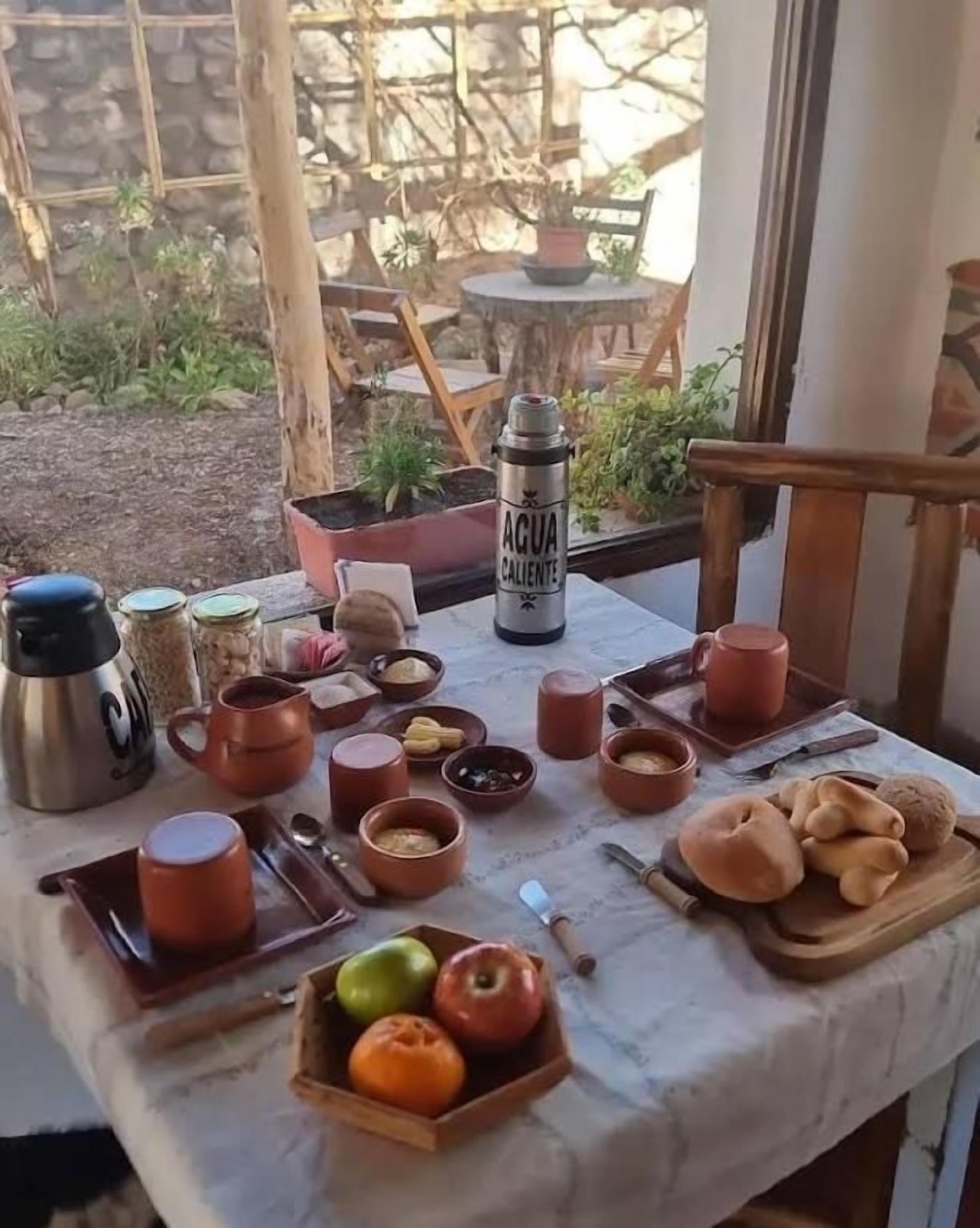 An outdoor dining area with a table set for breakfast, including fruits, bread, and various breakfast items.