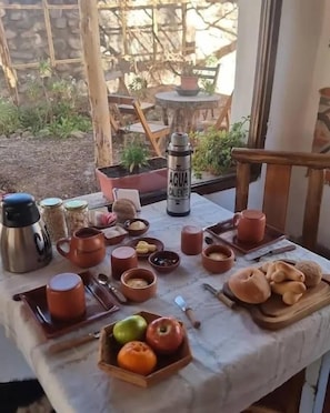 Un área de comedor al aire libre con una mesa dispuesta para el desayuno, incluyendo frutas, pan y diversas opciones para el desayuno.