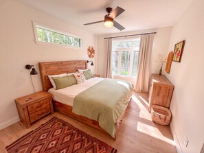 Una camera da letto con un letto in legno, un comodino, una ventola a soffitto, una finestra con tende e una lampada a parete.