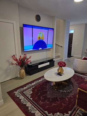 En stue med et fladskærms-tv, et sort multimøbel, et rundt sofabord og en rød gulvtæppe med et mønster.