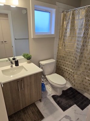 Un bagno con un lavandino bianco, un water, una piccola finestra sopra il water e una tenda da doccia con motivo geometrico.