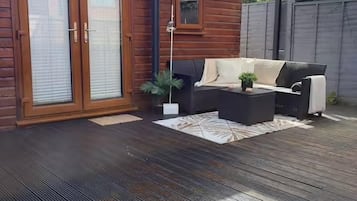 A wooden deck with a sofa and coffee table, a covered patio area, and a sliding glass door.