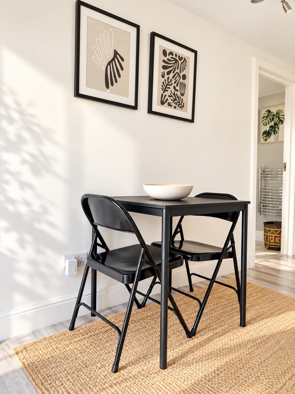 A dining area with a black table and chairs, a bowl on the table, and two framed artworks on the wall.