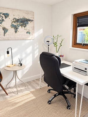A modern office space with a desk, chair, lamp, world map, potted plant, and printer.