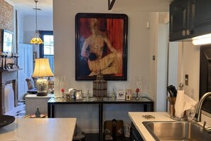 A kitchen with a central island, a hanging painting, and a variety of kitchen items. - Charming uptown New Orleans retreat (New Orleans)