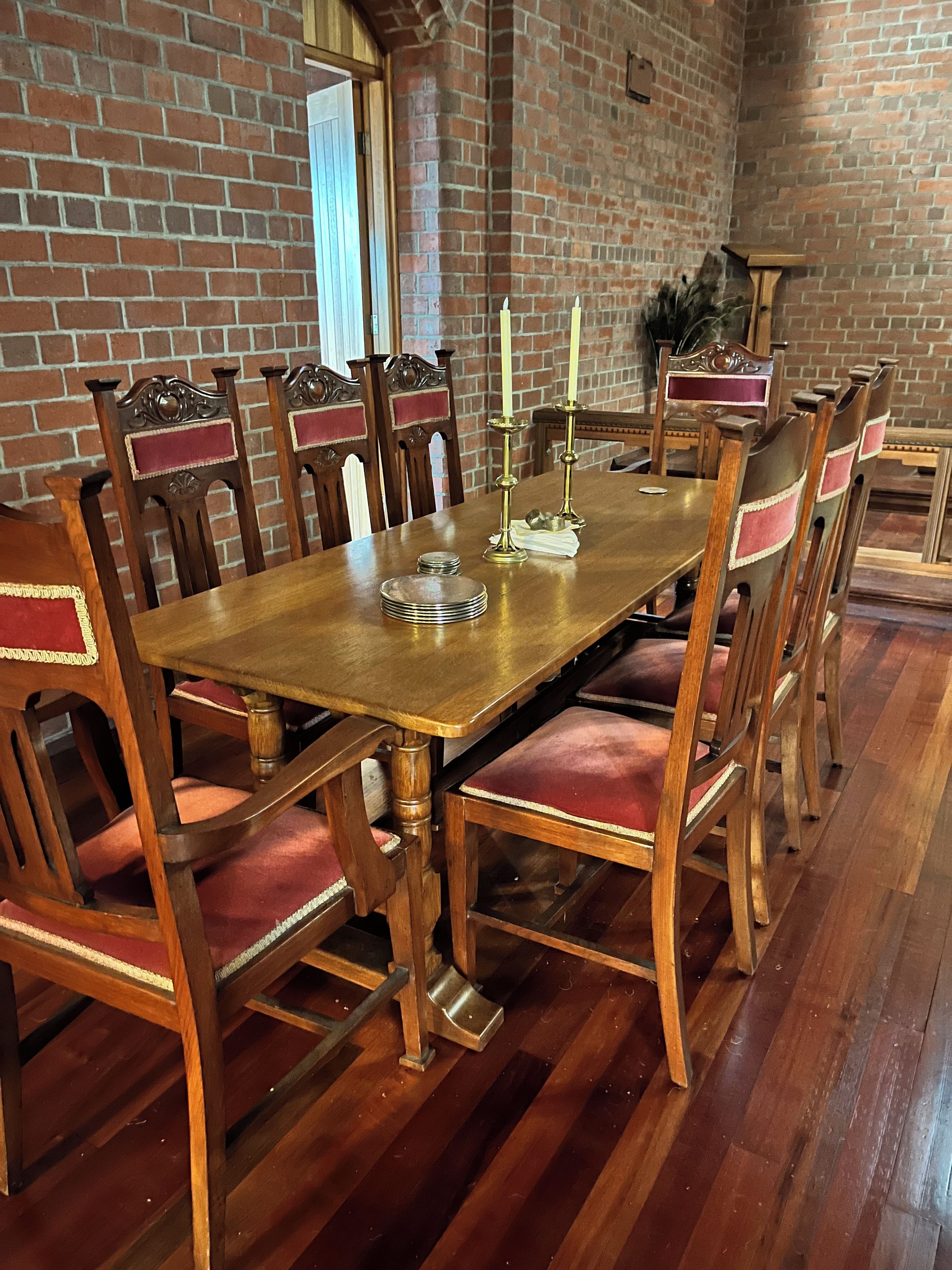 Un coin repas avec un mur en briques, des chaises en bois dotées de coussins rouges, une table en bois et deux bougies.