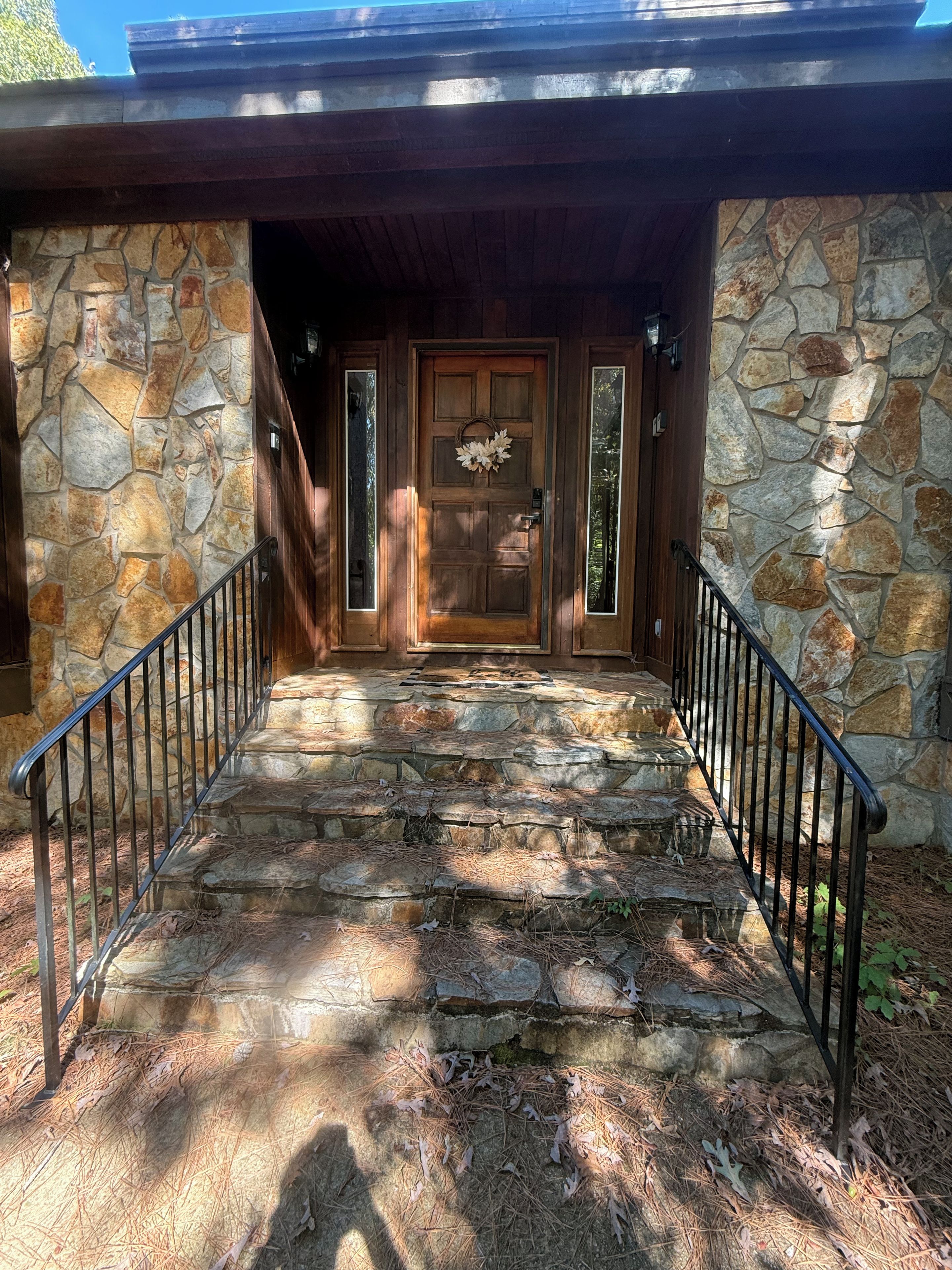 A stone staircase leading to a wooden door with a wreath, surrounded by stone walls and metal railings.