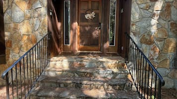 A stone staircase leading to a wooden door with a wreath, surrounded by stone walls and metal railings.