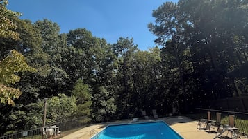 Una piscina rectangular con superficie de agua azul cristalina, rodeada por una solana de hormigón y una valla de metal.