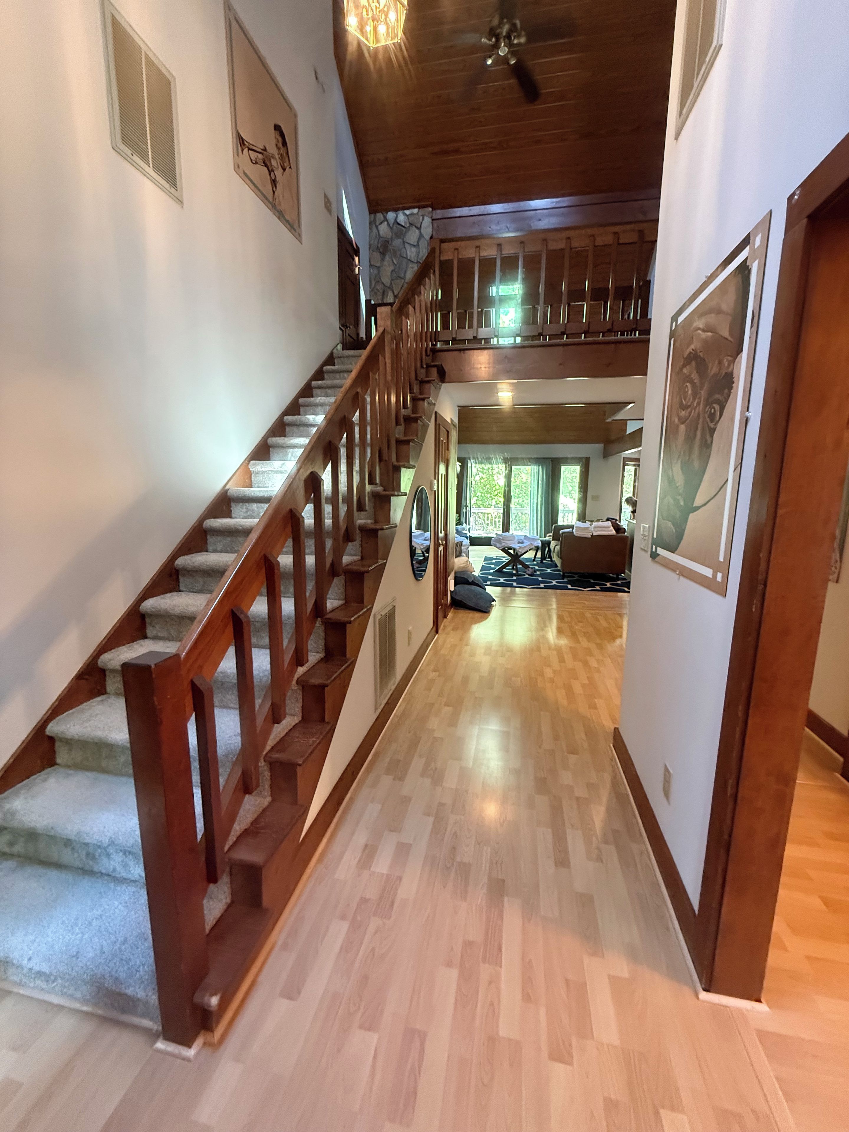 Una escalera de madera que conduce a un segundo piso, un pasillo con piso de madera y un comedor con mesas y sillas.