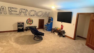 A room with a dartboard, a television mounted on the wall, and a ceiling fan.