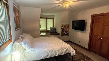 A bedroom with a bed, a bedside lamp, a television, a wooden door, and a ceiling light fixture.