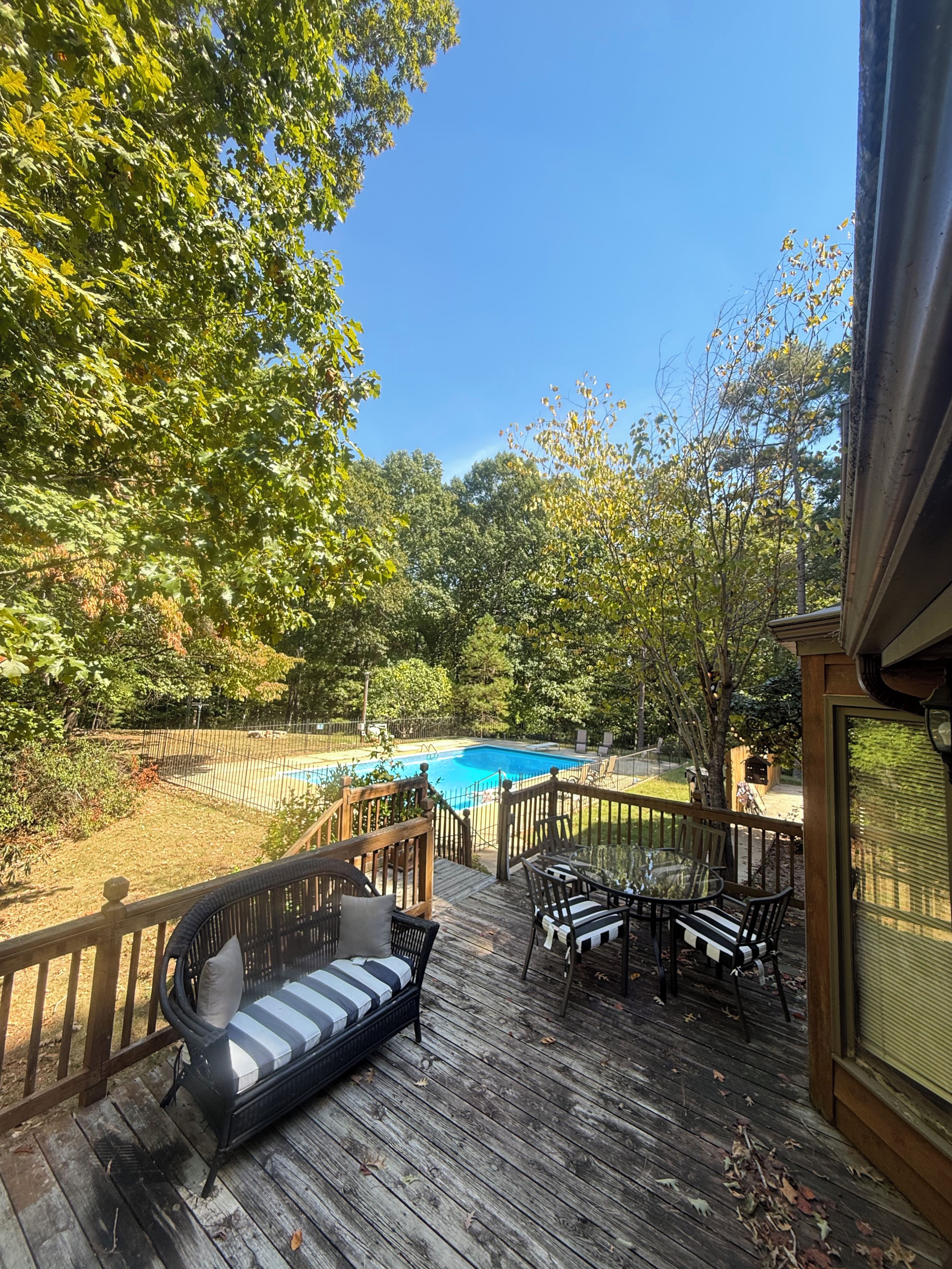 A wooden deck with a pool, surrounded by trees and a fenced area.