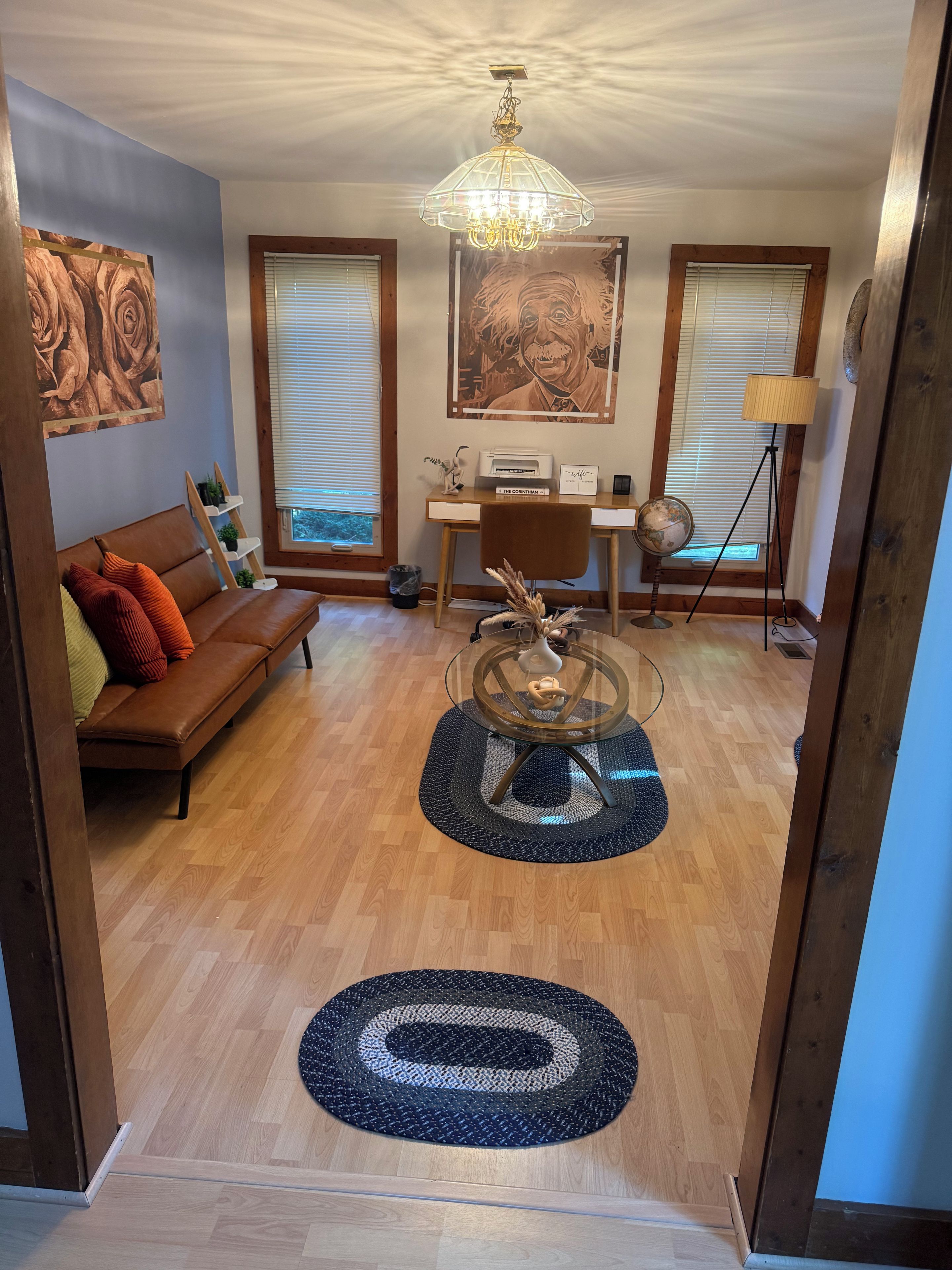 Una sala de estar con un sofá de cuero marrón, una mesa de centro de vidrio y piso de madera.