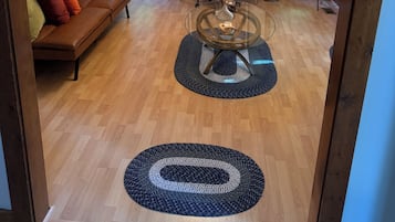 Una sala de estar con un sofá de cuero marrón, una mesa de centro de vidrio y piso de madera.