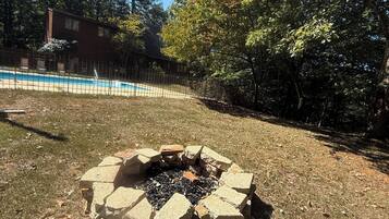 Un jardin avec un foyer extérieur, une piscine et une terrasse en bois.
