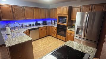 A modern kitchen with wooden cabinets, granite countertops, a built-in oven, and a stainless steel refrigerator.