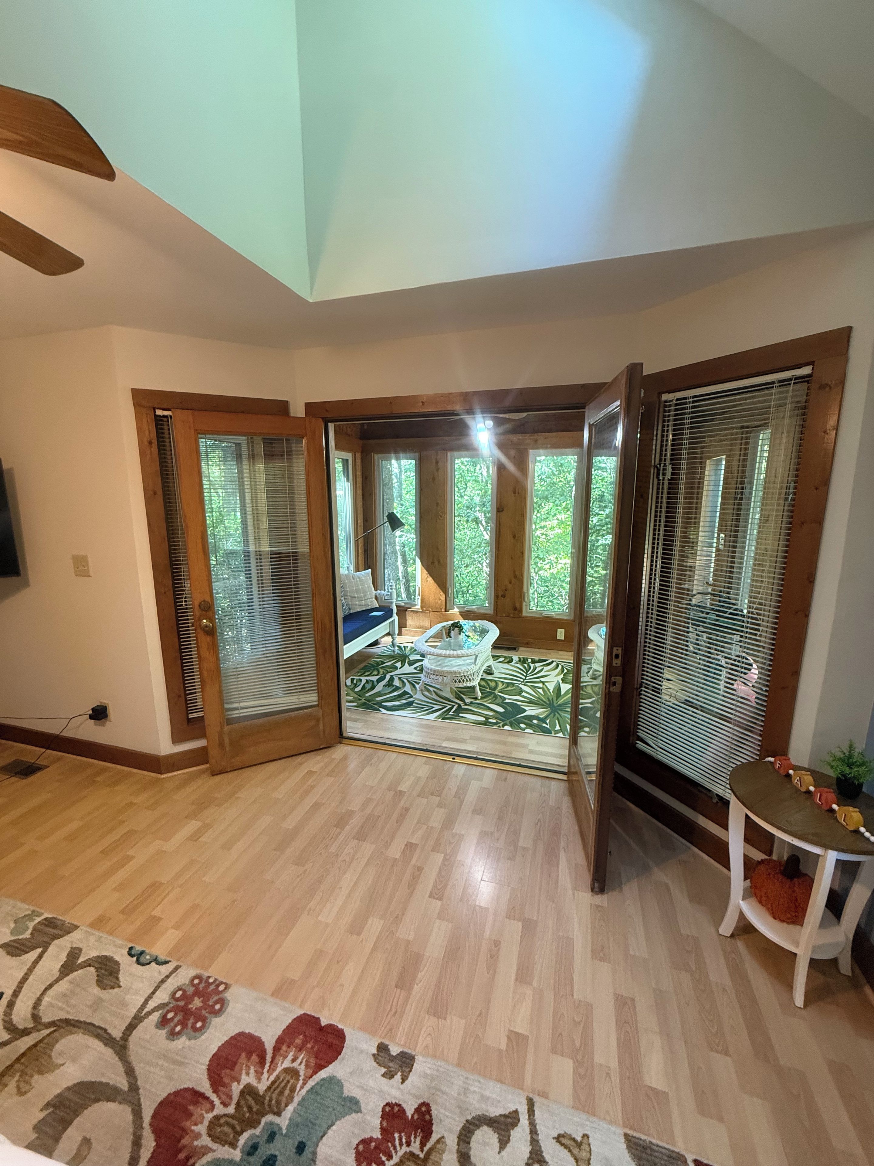 A room with a wooden floor, a patterned rug, a white chair, and a small table with a plant.