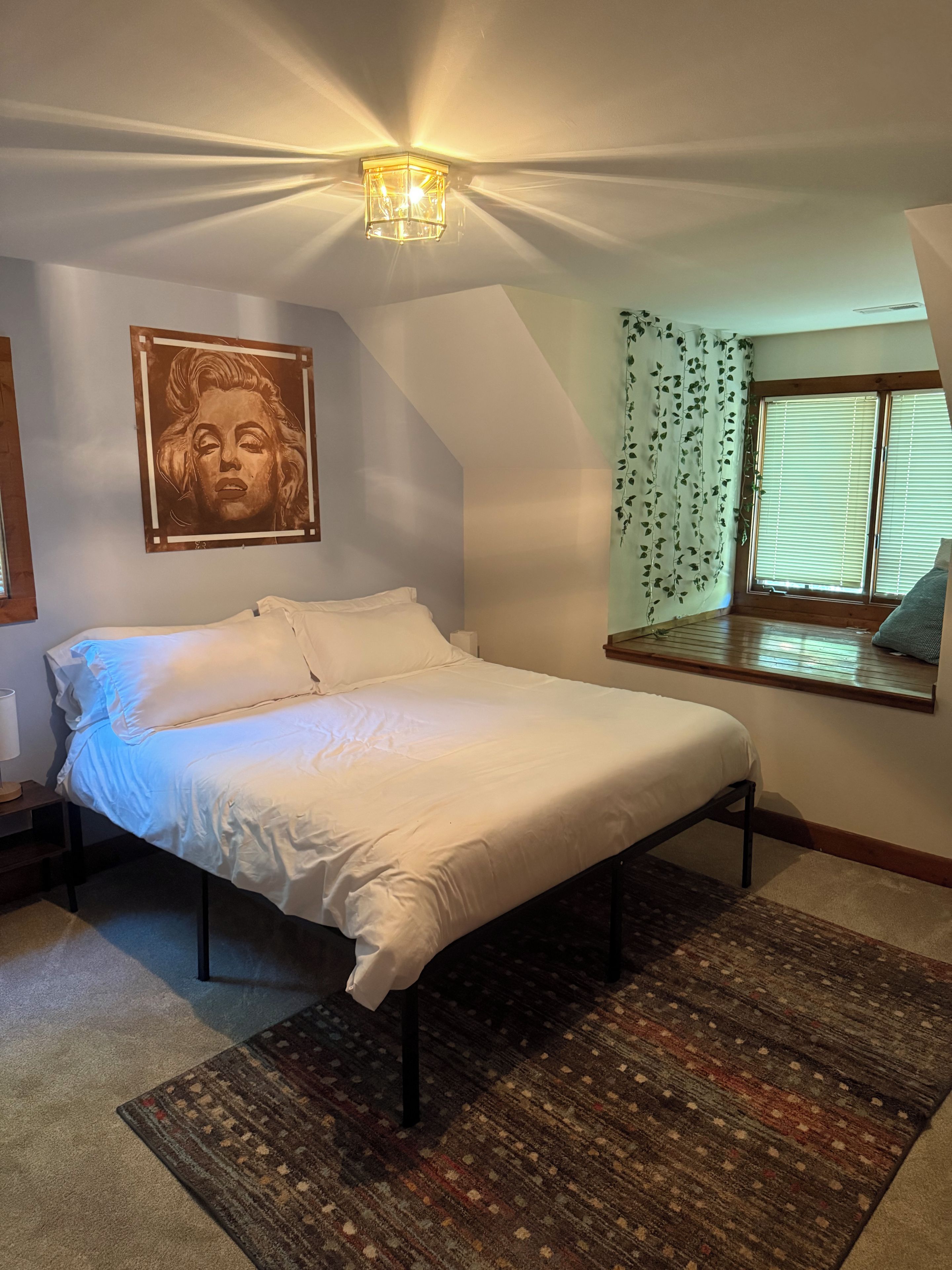 A bedroom with a bed, a wall-mounted artwork, a window with curtains, and a ceiling light fixture.