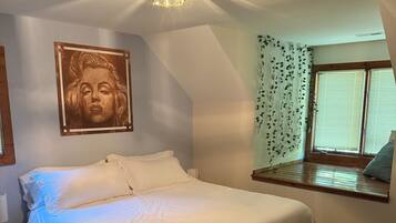 A bedroom with a bed, a wall-mounted artwork, a window with curtains, and a ceiling light fixture.