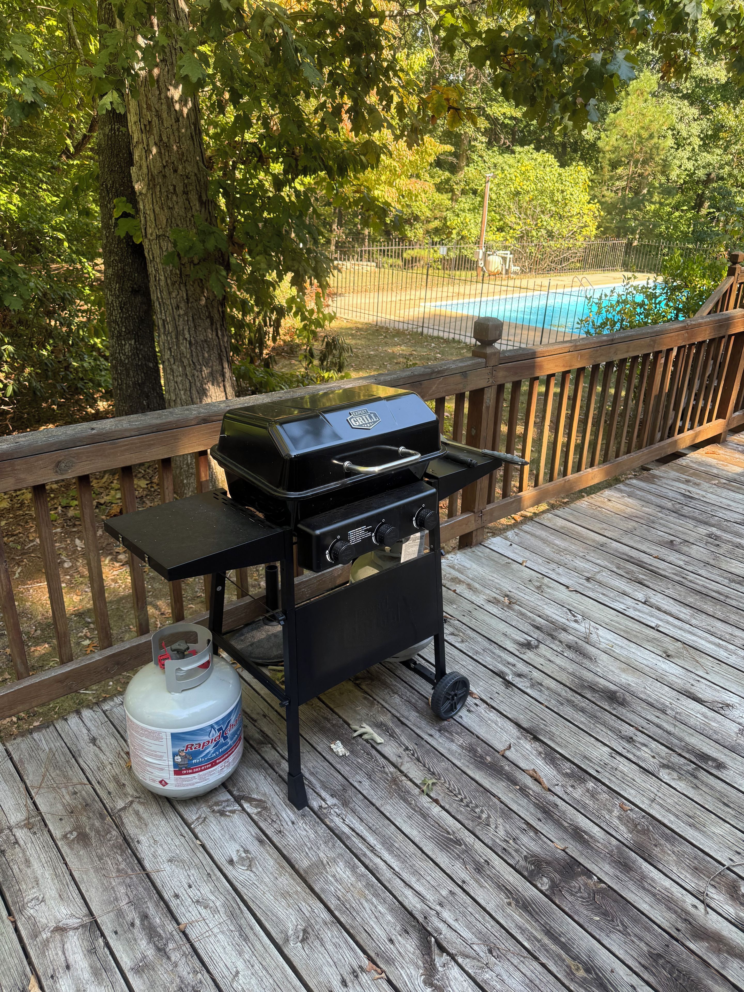 Una parrilla para barbacoa en una terraza de madera, con un tanque de propano cerca.
