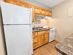 Una cocina con armarios de madera, un refrigerador blanco, una estufa y una encimera de granito.