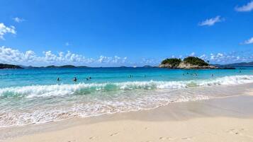 Une plage avec une eau d’un bleu limpide, des gens qui se baignent et une rive sablonneuse.