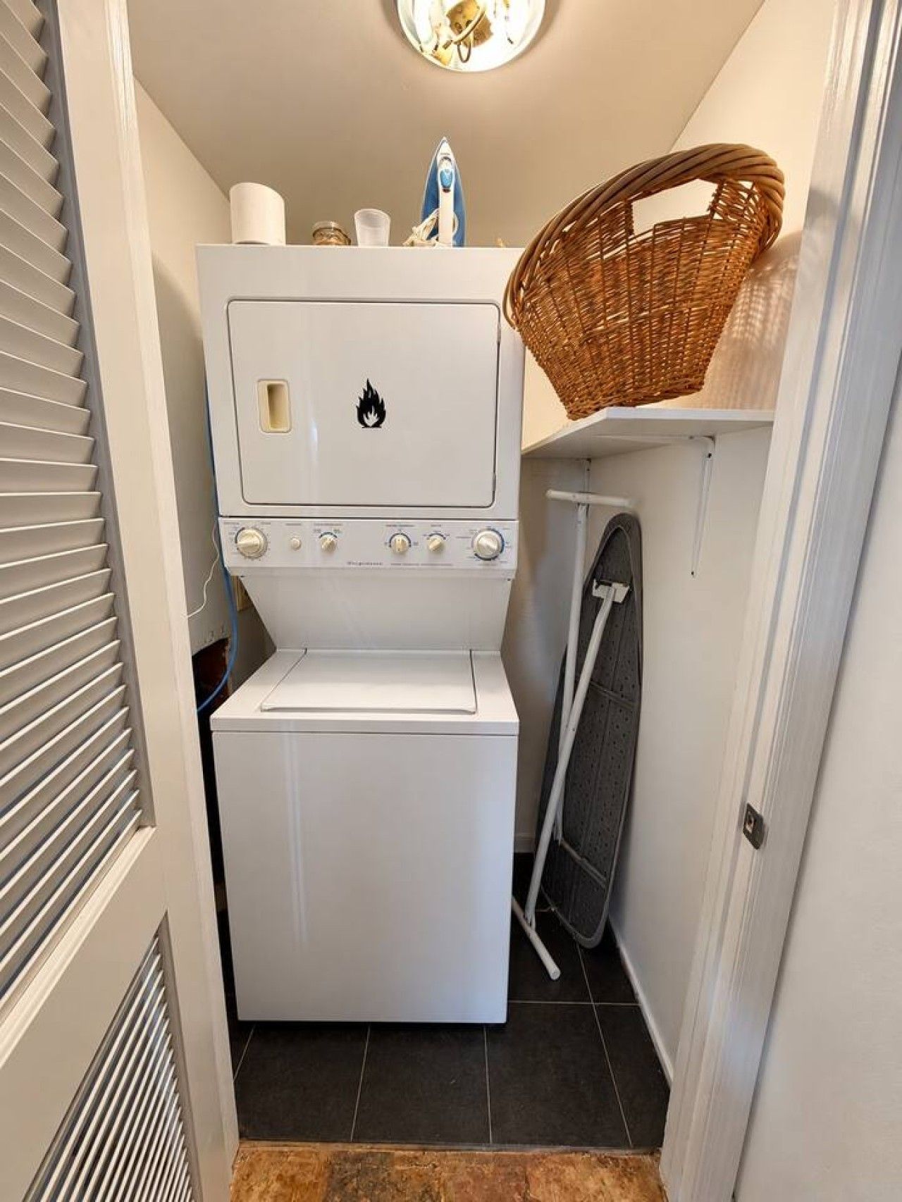 Een kleine wasruimte met een gestapelde wasmachine en droger, een mand aan de muur en een handdoekrek.
