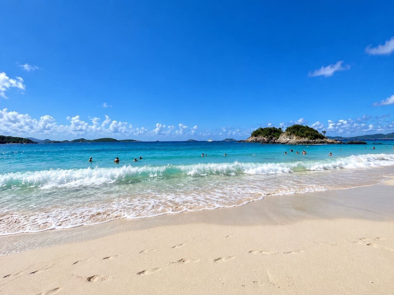 Ein Strand mit klarem türkisblauem Wasser, einem Sandstrand und einer kleinen Insel in der Ferne.