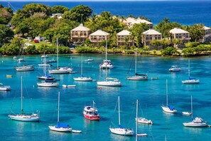 A coastal area with multiple sailboats docked in a marina, surrounded by lush greenery and a backdrop of buildings. - King’s Lighthouse | Garden Retreat, Downtown (Charlotte Amalie)