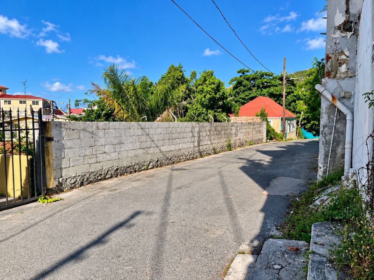 A narrow street with a stone wall on one side and a gated entrance on the other.