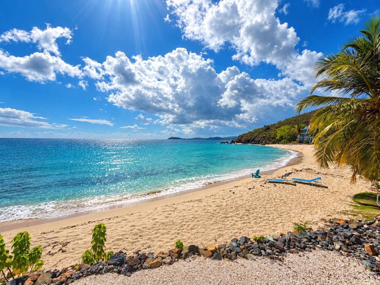 Une plage avec une eau turquoise et limpide, un rivage sablonneux et quelques chaises longues.
