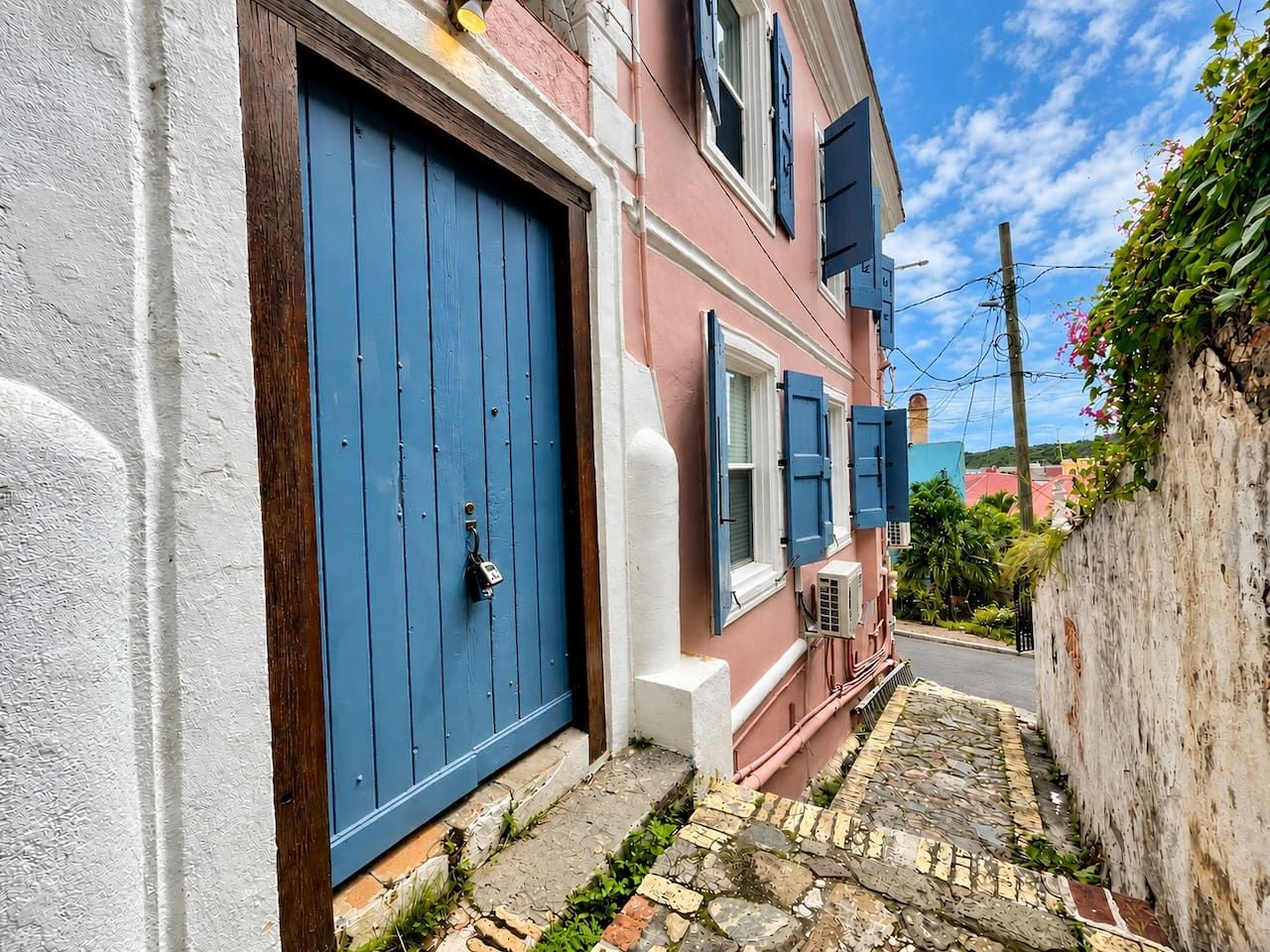 A narrow alleyway with a pink building, a blue door, and a white wall.