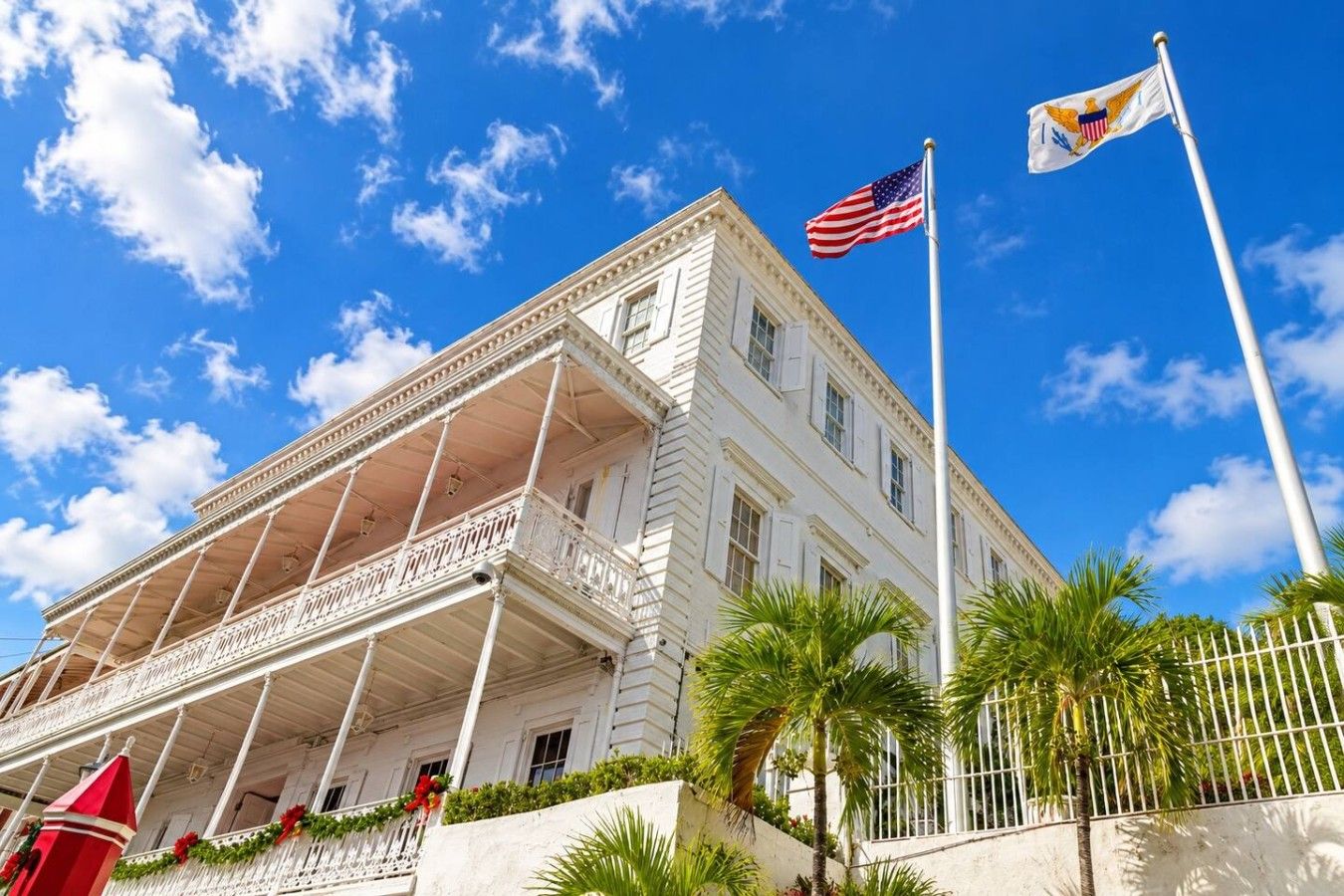 A white building with a balcony, an American flag, and a flag with a blue field and a gold eagle.