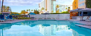 A swimming pool with lounge chairs and umbrellas, surrounded by palm trees and hotel buildings. - Resort 1 bedroom in Anaheim for National Association of Music Merchants - NAMN (Anaheim)