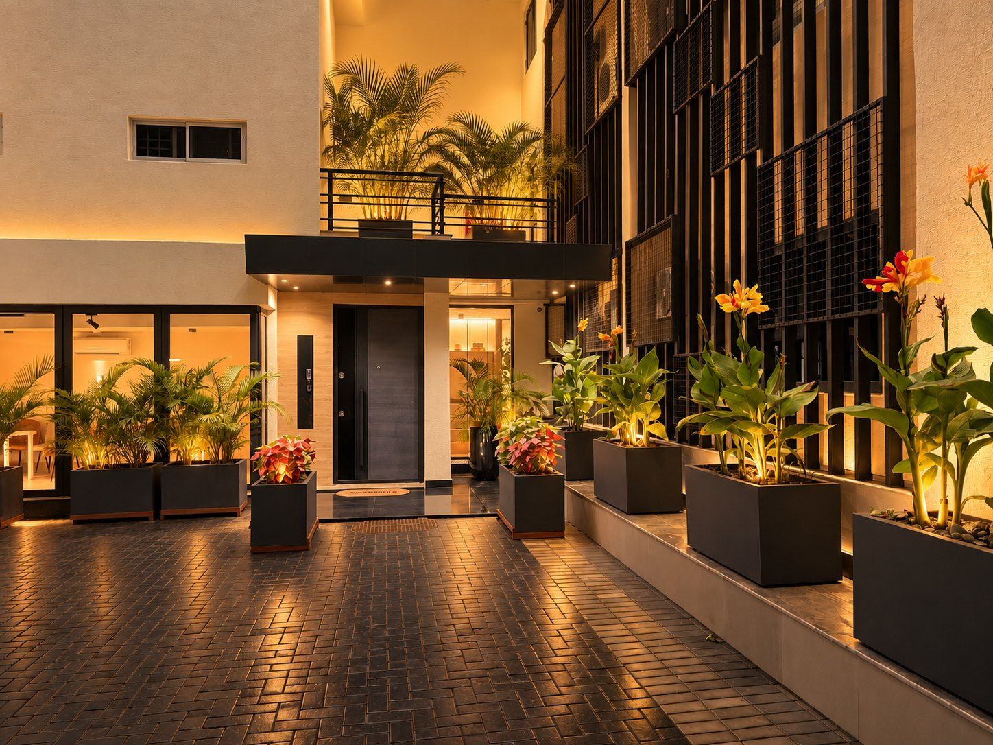 Un patio de hotel con un camino pavimentado, plantas en macetas y fachada de un edificio moderno.