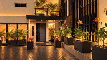 Un patio de hotel con un camino pavimentado, plantas en macetas y fachada de un edificio moderno.