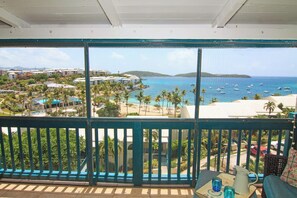A balcony with a view of a beach, palm trees, and boats on the water. - Luxury Island Escape 3BR, Panoramic Views, AC, Pool, Free Concierge, & Generator (St Thomas)