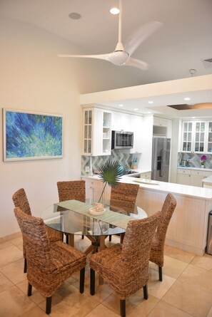 A modern kitchen with white cabinetry, a glass dining table, wicker chairs, and a ceiling fan. - Luxury Island Escape 3BR, Panoramic Views, AC, Pool, Free Concierge, & Generator (St Thomas)
