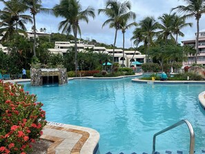 A swimming pool with a stone waterfall feature, surrounded by palm trees and a building with balconies. - Luxury Island Escape 3BR, Panoramic Views, AC, Pool, Free Concierge, & Generator (St Thomas)