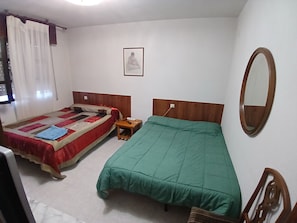 A bedroom with two beds, a bedside table, a mirror, and a framed picture on the wall.