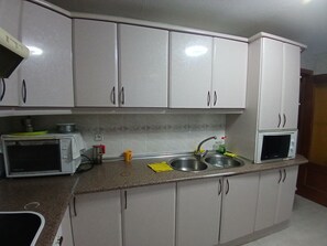 A kitchen with white cabinets, a microwave, a sink, and a kettle.