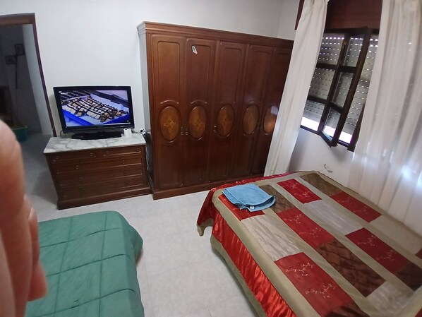 A bedroom with a bed, a wardrobe, a television on a stand, and a window with curtains.