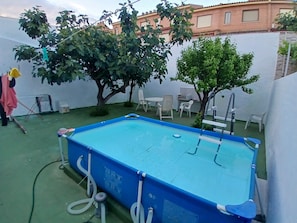 A swimming pool with a ladder, surrounded by a white wall and a tree.