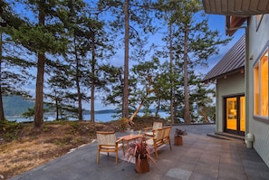 A patio with a table and chairs, surrounded by tall trees and a view of a lake. - Private Luxury 4 Bedroom Estate on 4 Acres with over 1,100 feet of shoreline! (Orcas)