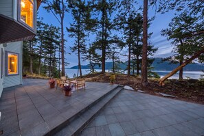 A house with a patio overlooking a lake, surrounded by tall trees. - Private Luxury 4 Bedroom Estate on 4 Acres with over 1,100 feet of shoreline! (Orcas)