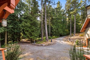A forested driveway leading to a building with a stone border and a gravel path. - Private Luxury 4 Bedroom Estate on 4 Acres with over 1,100 feet of shoreline! (Orcas)