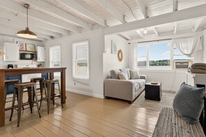 Un espacio habitable moderno con zona de cocina, área de estar con sofá y sillones, y un ventanal que ofrece vistas.