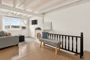 A living room with a sofa, a bench, a TV, and a window with curtains. - Keuka Lakefront - 2 Homes Captain's Quarters & Crow's Nest - Hot Tub/Kayaks/SUPs (Penn Yan)